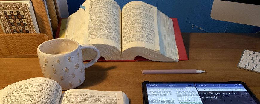 Stilleben aus aufgeschlagenen buch, daneben ein Tablet mit Tafelbild und Text, eine Tasse und ein weiteres Buch