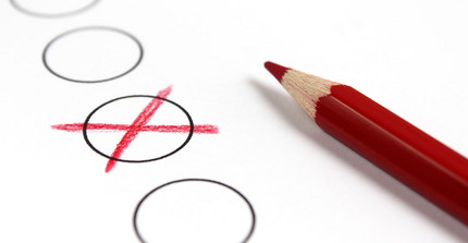 Wahlhaken: Rotes Kreuz in einem der Kreise auf einem weißen Blatt Papier, rechts daneben liegt ein roter Stift.