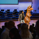 Drei Personen vom Zentrum für Hochschulsport und Feel Good Campus stehen auf der Bühne, wovon eine Person ein Dinosaurier-Kostüm trägt. Sie animieren die Studierenden zum Sport.