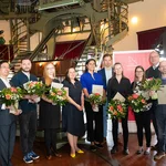 Mehrere Personen mit Urkunden und Blumensträußen posieren für ein Foto.