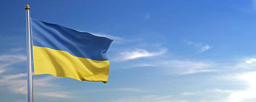 Auf dem Foto ist die wehende urkrainische Flagge zu sehen, im Hintergrund blauer Himmel. Das Foto ist von AdobeStock/Negro Elkha.