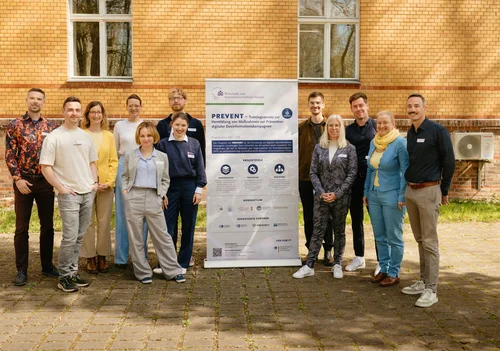 Gruppe von Personen vor einem Poster, das PREVENT zeigt.