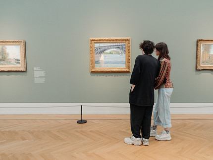Zwei Personen schauen sich ein Gemälde in einer Ausstellung an