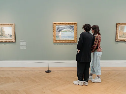 Zwei Personen schauen sich ein Gemälde in einer Ausstellung an