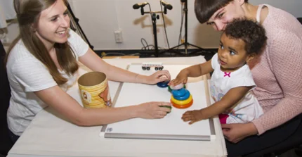 Mother and child are sitting at a table and playing with toys with the experimenter