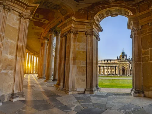 Blick aus einem halbrunden Säulengang auf ein historisches Nebengebäude des Neuen Palais