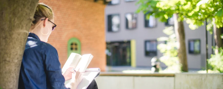 Studierende liest ein Buch auf einer Wiese