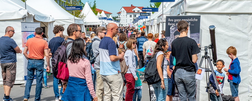Menschen auf einer Veranstaltung, im Hintergrund große eiße Zelte