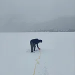 Field site Leutasch: Scientist laying out measuring tape in the snow, with faint silhouettes of mountains in the foggy background | Photo: Cosmic Sense Consortium