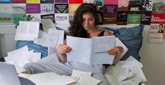 Junge Frau liest in einem Heft auf einem Bett voller Papiere. Foto: Sophia Pakzad