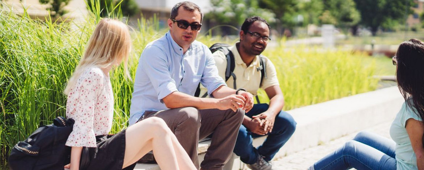 Studierende sitzen auf dem Campus Golm auf einer Bordsteinkante. Hinter ihnen ist eine Wiese zu sehen.