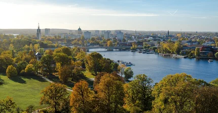 Man sieht die Stadt Potsdam aus der Vogelperspektive. Im Vordergrund sind Bäume sowie die Havel, im Hintergund erhebt sich die Skyline der Stadt.
