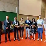Auf dem Bild stehen die Ehrengäste der Podiumsdiskussion zum 30-jährigen Jubiläum des Studiengangs lächelnd nebeneinander – in den Händen halten sie Blumensträuße.