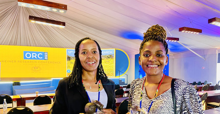 Smiling NamTip researchers holding prizes in their hands with a conference hall in the background