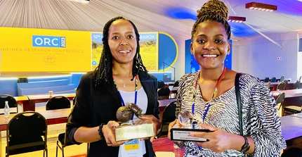 Smiling NamTip researchers holding prizes in their hands with a conference hall in the background