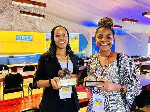 Smiling NamTip researchers holding prizes in their hands with a conference hall in the background