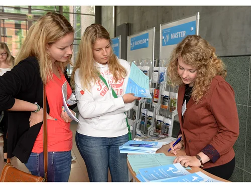 Zwei junge Frauen lassen sich von einer weiteren jungen Frau an einem Stehtisch beraten