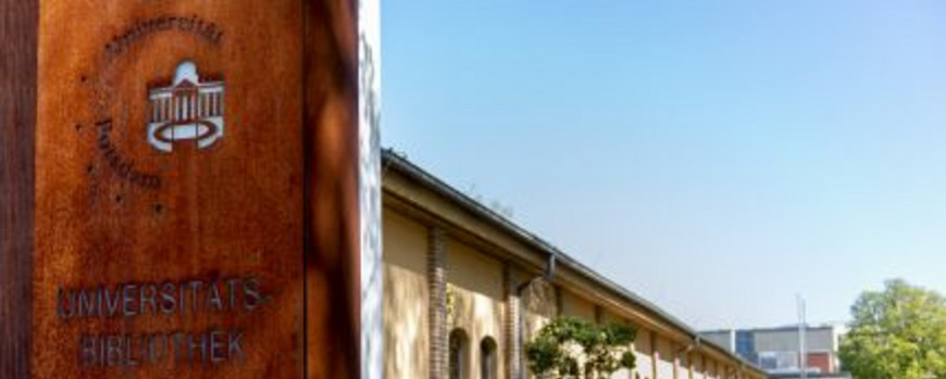 Flaches, langgestrecktes Gebäude, links im Vordergrund Metallsäule mit Schriftzug "Universitätsbibliothek Bereichsbibliothek Babelsberg"