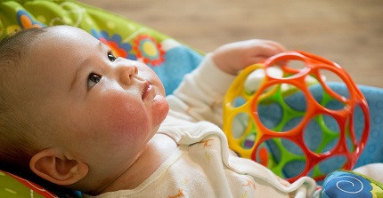 Ein Baby liegt auf einer Decke mit einem Spielzeug in der Hand und schaut nach oben.