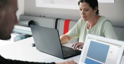 Ein Mann und eine Frau sitzen sich gegenüber, beide sitzen an einem Laptop.