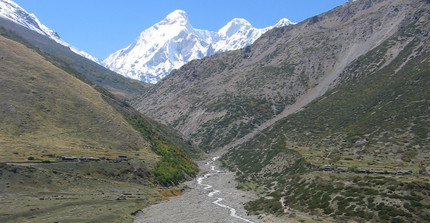 Ein Fluss im westlichen Himalaya transportiert Sediment aus dem Gebirge. Im Hintergrund sind schneebedeckte, hohe Berge zu sehen.