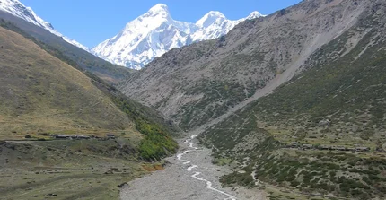Ein Fluss im westlichen Himalaya transportiert Sediment aus dem Gebirge. Im Hintergrund sind schneebedeckte, hohe Berge zu sehen.