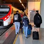 Menschen mit Koffern auf einem Bahnsteig, neben ihnen ein wartender Zug.