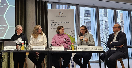 Fünf Personen sitzen an einem langen Tisch.