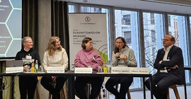 Fünf Personen sitzen an einem langen Tisch.