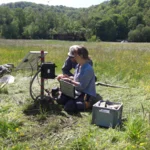 Photo of two people installing electronics & a solar panel for soil moisture sensors on a meadow | photo: Cosmic Sense Consortium