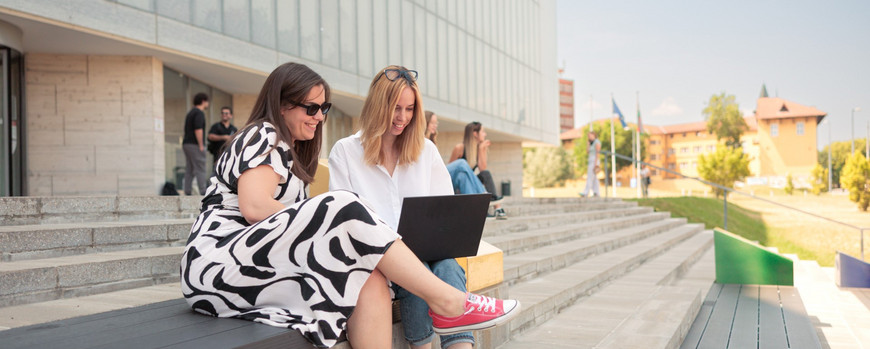 EDUC R&I Fellowships Zwei Personen sitzen auf einer Treppe und schauen gemeinsam in einen Laptop.