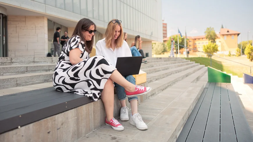 Two persons sitting on stairs looking into a laptop.