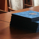 Ein Stapel mit mehreren dunkelblau samtenen Urkundenmappen liegt auf einem Holztisch.