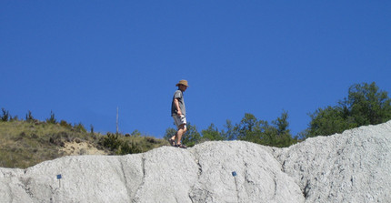 Ein Mann in kurzer Hose und mit Hut geht auf einem Gebirgsrand entlang