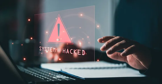 Laptop mit Schriftzug "System hacked" und eine Hand auf der Tastatur