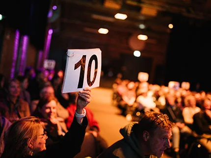 Blick ins Publikum beim Science Slam. Eine "10" wird im Vordergrund hochgehalten.