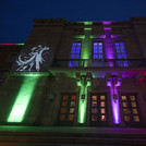 Eine Hausfront im Halbdunkel, die mit bunten Lichtern angestrahlt wird