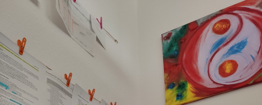 Ein Laptop und ein Drucker auf einem tisch. an der Wand hängenausgedruckte Notizen und ein buntes Bild mit abstrakten Mustern