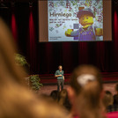 Eine Person auf der Bühne, im Hintergrund eine Powerpointpräsentation mit Lego-Figur