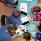 Aufnahme von oben von einem Tisch an dem Kinder ihre Kuscheltiere in eine Teddyklinik geben.