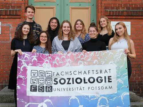 Mehrere Personen halten ein Banner vor einer Ziegelwand