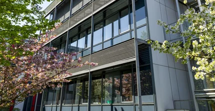 Fassade aus Stahl und Glas eines Forschungsgebäudes, davor zwei Bäume