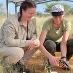 NamTip researchers sitting in front of an opened Diviner probe (white pipe emerging from the soil) under the roof of the TipEx experiment