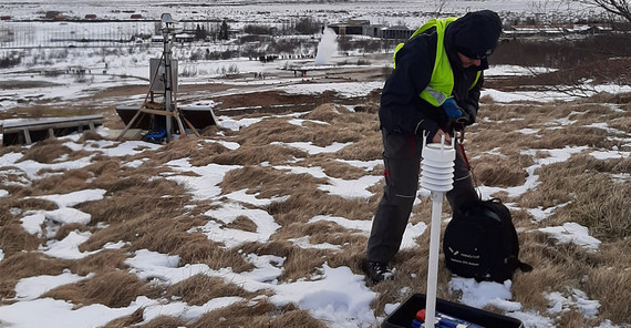 Daniel Vollmer installs a weather station (Thomas Walter, GFZ) on top of a hill northwest of Strokkur. Eruption of Strokkur visible in the background. | Photo: Eva Eibl