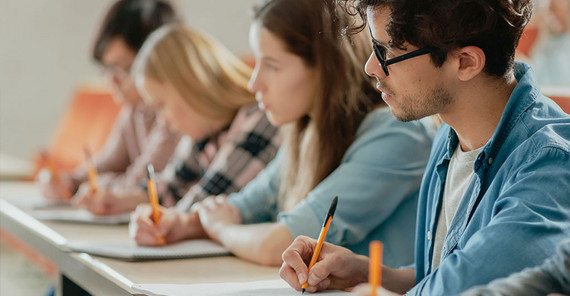 Studierende sitzen in einer Bankreihe im Seminarraum. Das Foto ist von AdobeStock/Gorodenkoff.