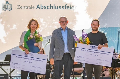 3 Personen mit 2 großen symbolischen Schecks
