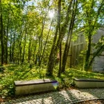 Zwei Bänke vor Bäumen, dahinter das Portal eines großen Hauses