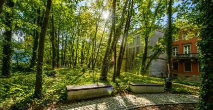 Two benches in front of trees, behind them the portal of a large house