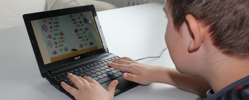 A child is sitting at a table and is looking to a tablet. The fingers are laying on the keyboard.