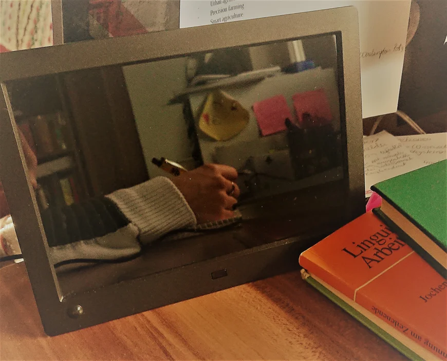 Bücher auf Schreibtisch. Reflexion einer schreibenden Hand in einem digitalen Bilderrahmen